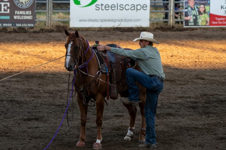 A cowboy wearing a hat prepares to mount his horse during a rodeo event, showcasing Western culture.