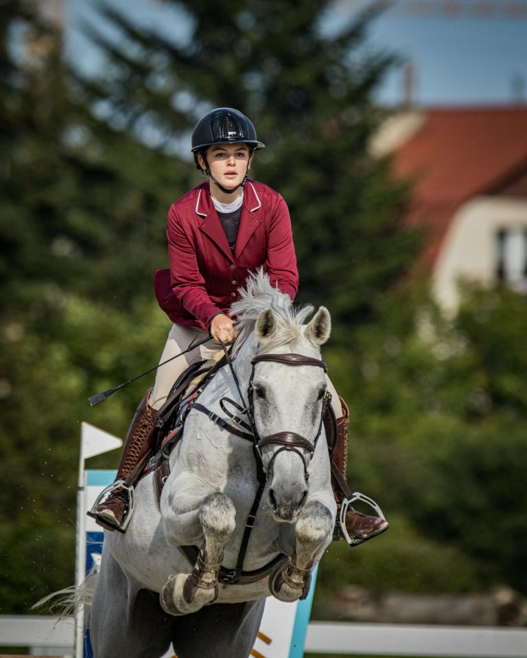 A skilled female equestrian riding a white horse during a jumping competition.