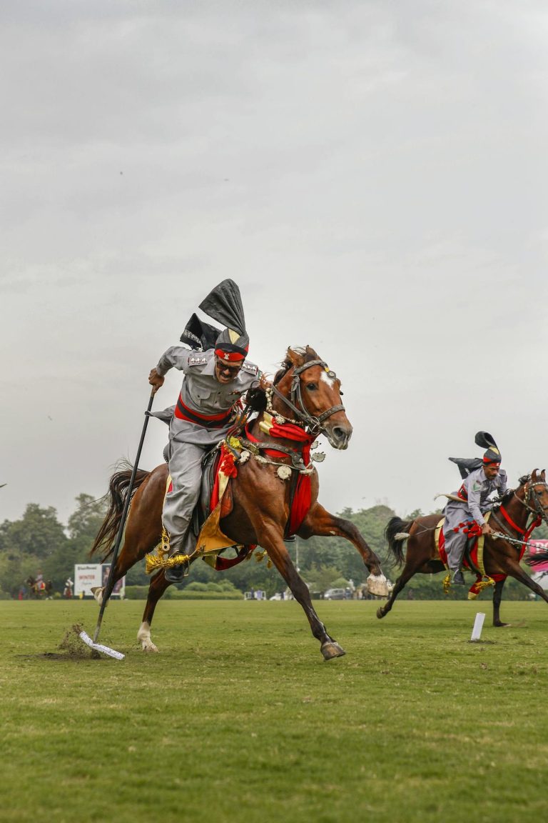Action-packed scene of men on horses in traditional attire, showcasing skill and speed in an outdoor event.