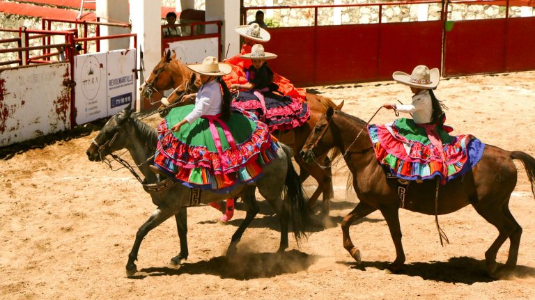 Vibrant charrer&iacute;a scene featuring women on horseback in traditional attire.